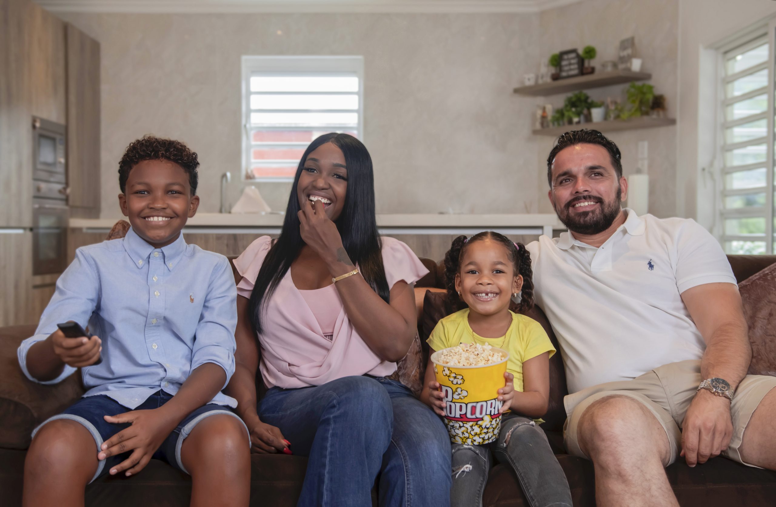 Man, woman, son and daughter are on the couch with popcorn and a tv remote